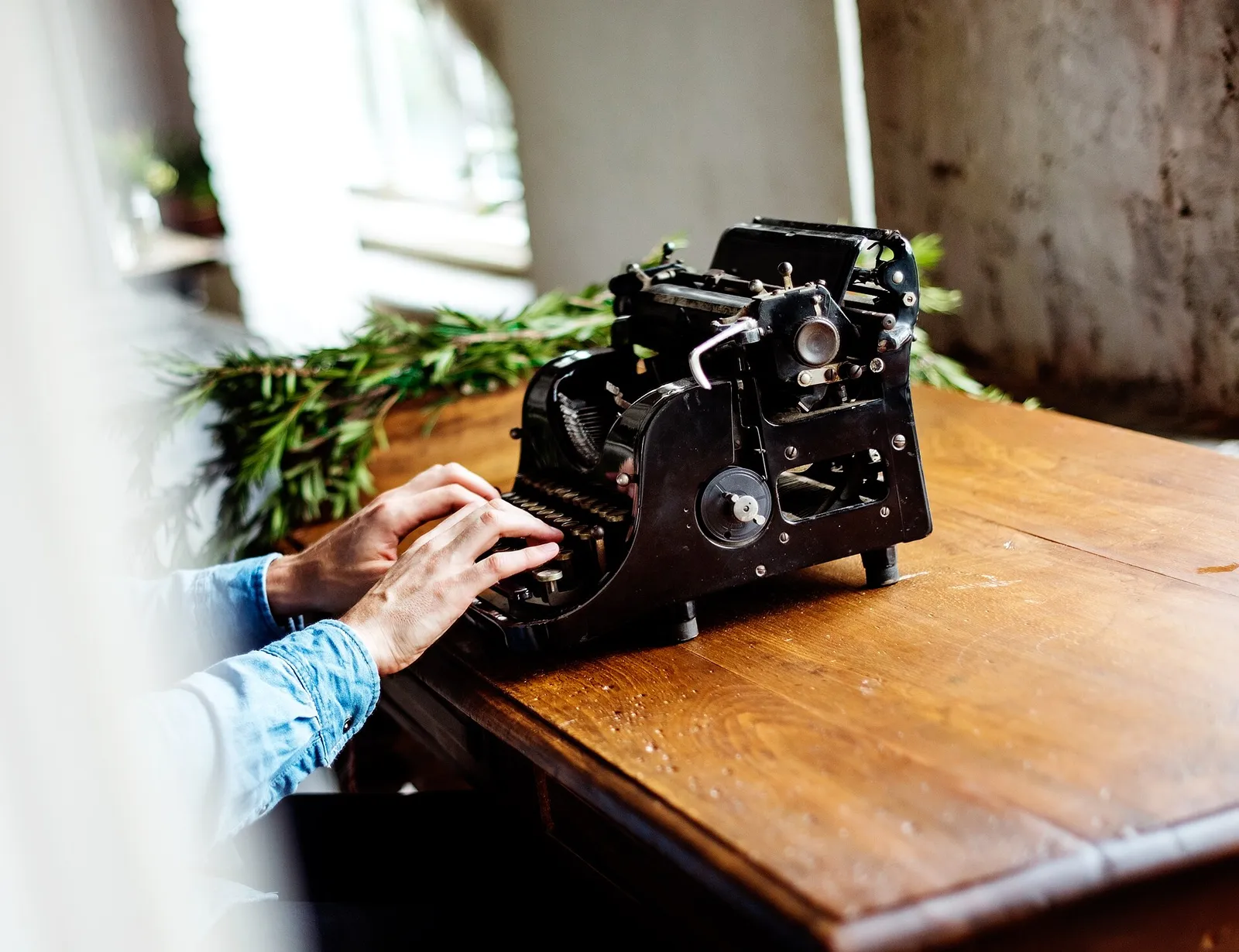 A hand at a typewriter on a wooden desk